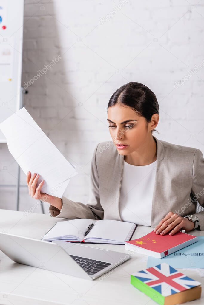 concentrated translator holding document near empty notebook and laptop