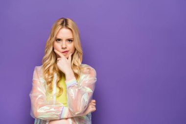 Mor arka planda, renkli kıyafetli, dalgın sarışın genç kadın.