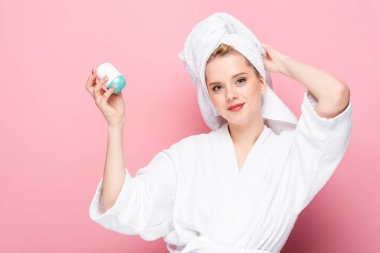 Kafasında havluyla bornozlu genç bir kadın pembe deodorant taşıyor.