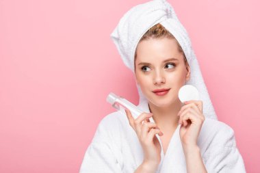 young woman in bathrobe with towel on head with micellar water and cotton pad isolated on pink clipart
