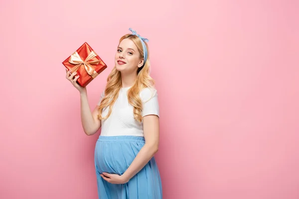 ブロンド若いです妊娠中の女性とともにギフトボックス上のピンクの背景 — ストック写真