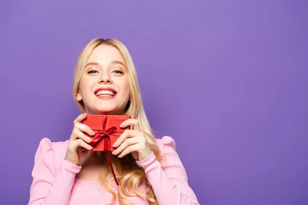 Happy Blonde Young Woman Holding Red Gift Box Purple Background — Stock Photo, Image