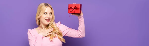 Happy Blonde Young Woman Holding Red Gift Box Purple Background — Stock Photo, Image