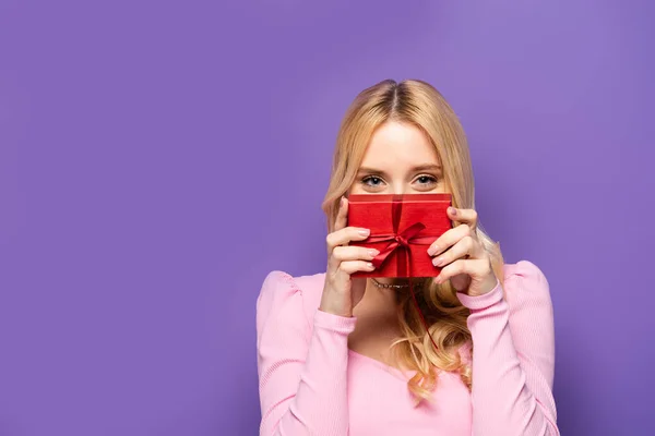 Jovem Loira Segurando Caixa Presente Vermelho Perto Rosto Fundo Roxo — Fotografia de Stock