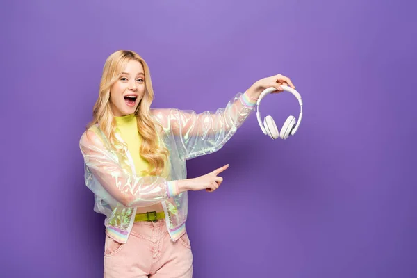 Excited Blonde Young Woman Colorful Outfit Pointing Headphones Purple Background — Stock Photo, Image