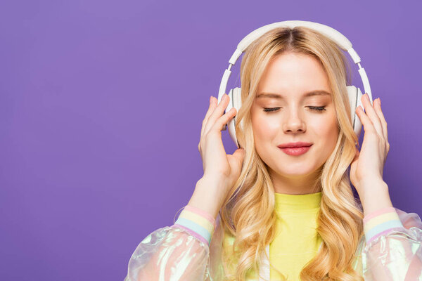 блондинка в красочном наряде и наушниках с закрытыми глазами, изолированными на фиолетовый