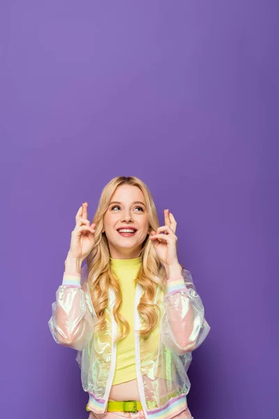 Happy Blonde Young Woman Colorful Outfit Crossed Fingers Purple Background — Stock Photo, Image