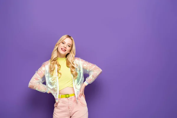 笑顔ブロンド若いです女性でカラフルな衣装で手でポーズの上に紫色の背景 — ストック写真