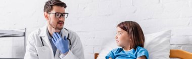 doctor pointing at throat while talking to child in hospital, banner