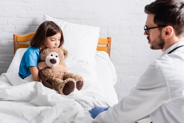 Sick Girl Teddy Bear Sitting Bed Doctor Blurred Foreground — Stock Photo, Image