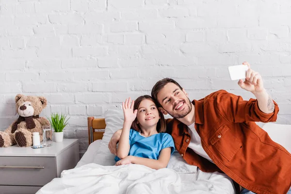 Sonriente Chica Saludando Mano Mientras Feliz Padre Tomando Selfie Smartphone — Foto de Stock