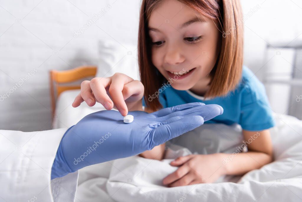 cheerful girl taking pill from pediatrician in hospital, blurred background