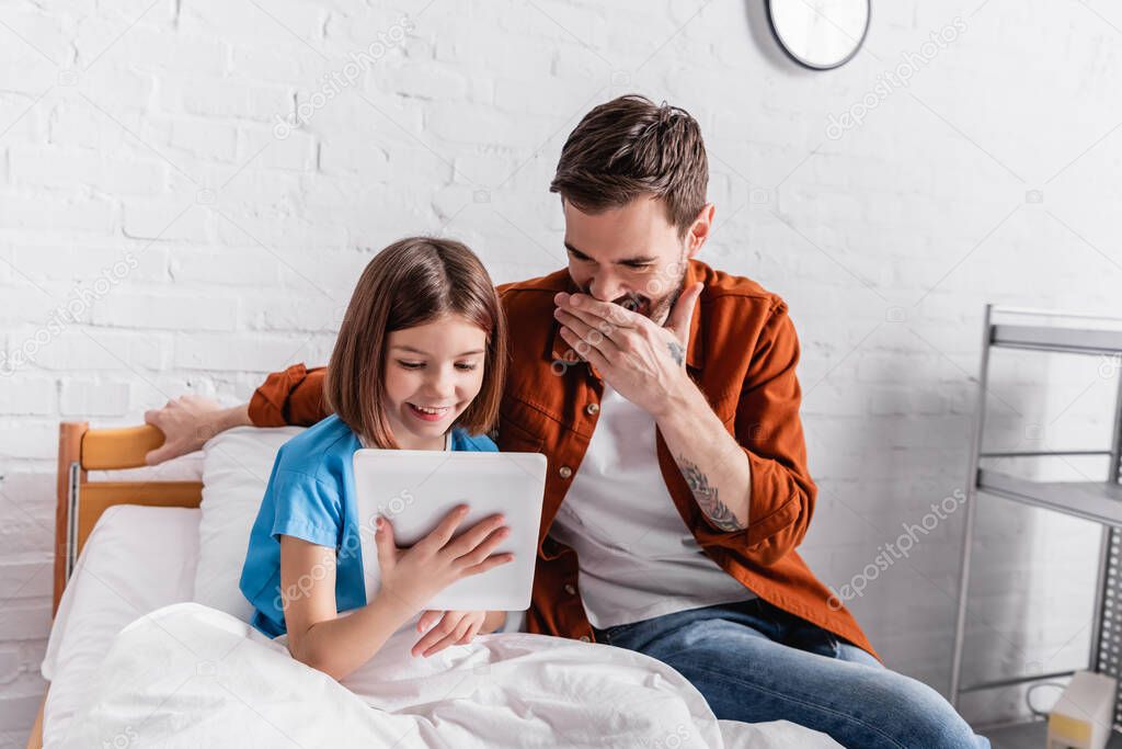 laughing girl with father using digital tablet in hospital