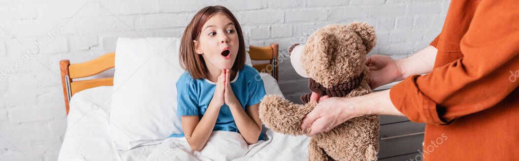 amazed girl showing wow gesture near dad with teddy bear in hospital, banner