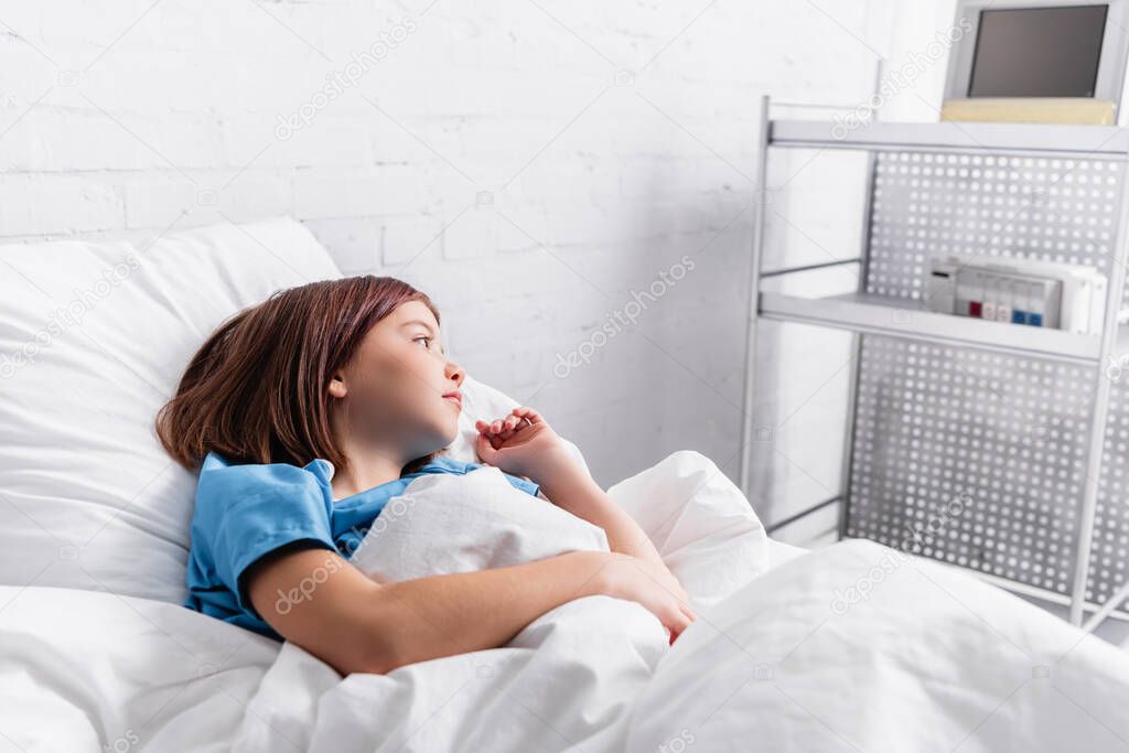 diseased girl looking away while lying in hospital bed