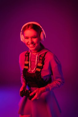 KYIV, UKRAINE - 27 Kasım 2020: Mor üzerinde joystick tutan kablosuz kulaklıklı neşeli kadın 