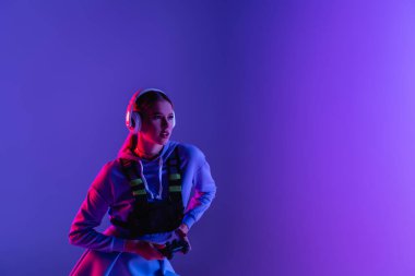 KYIV, UKRAINE - Kasım 27, 2020: Kablosuz kulaklıklı kadın oyun platformunu tutuyor ve mor renkte video oyunu oynuyor 