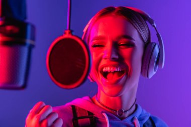 young singer in wireless headphones recording song while singing in microphone on blurred foreground  clipart