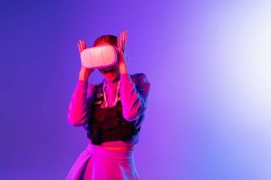Mor arka planda sanal gerçeklik kulaklığını ayarlayan genç bir kadın. 