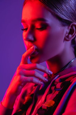 Genç düşünceli kadının yüzünde pembe ışık. Mor üzerine izole edilmiş dudaklara dokunuyor. 