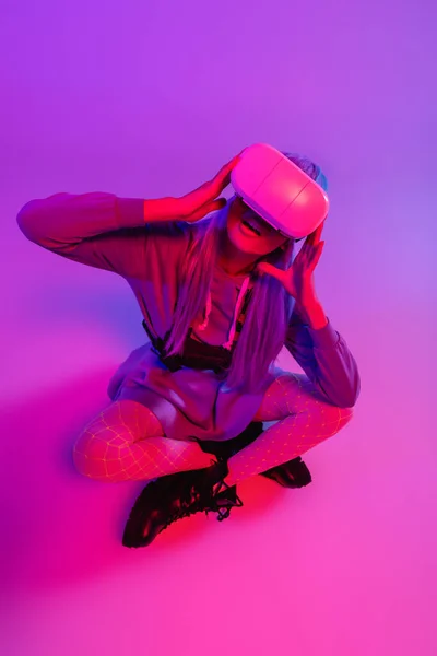 Удивленная Женщина Наушниках Виртуальной Реальности Сидит Скрещенными Ногами Фиолетовом — стоковое фото