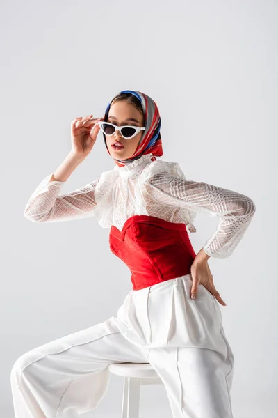 Stylish Woman Headscarf Adjusting Sunglasses Sitting Stool Hand Hip Isolated — Stock Photo, Image