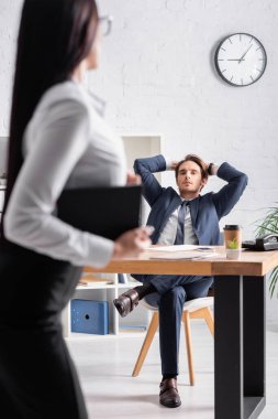 Önplandaki seksi sekretere bakarken elleri başının arkasında oturan iş adamı.