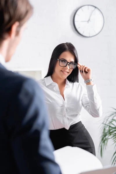 Flirty Brunette Secretary Touching Eyeglasses While Looking Businessman Blurred Foreground — Stock Photo, Image