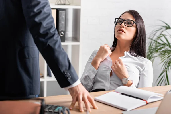 passionate secretary unbuttoning blouse while sitting at workplace near businessman