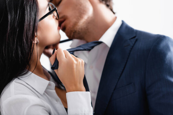 partial view of passionate couple of businesspeople kissing in office, blurred background