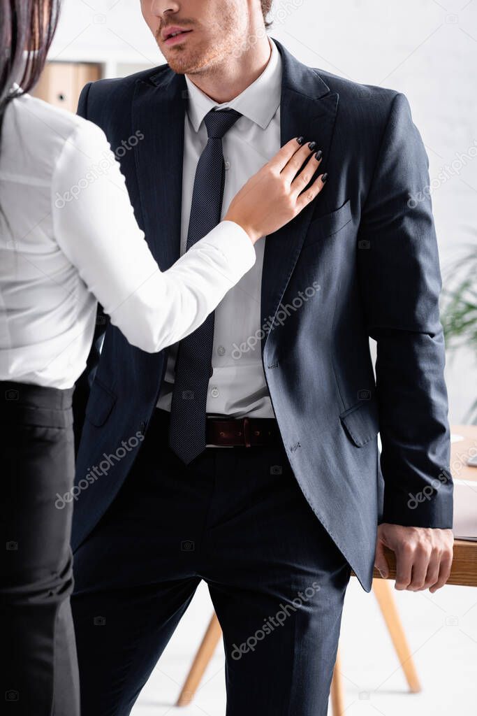 partial view of secretary touching suit of businessman while flirting with him in office