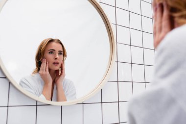 Kadınlar tuvalette aynaya bakarken yüzlerine dokunuyor.