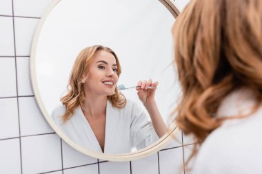 joyful woman holding toothbrush with toothpaste and looking at mirror clipart