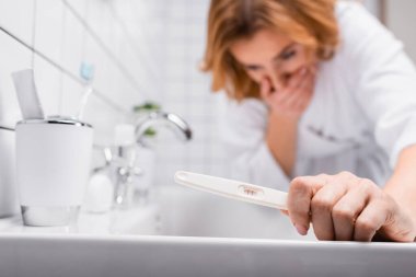 pregnancy test in hand on pregnant woman in bathrobe feeling nausea on blurred background clipart