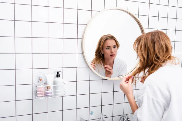 Mujer Preocupada Albornoz Ajustando Cabello Mientras Mira Espejo Baño — Foto de Stock