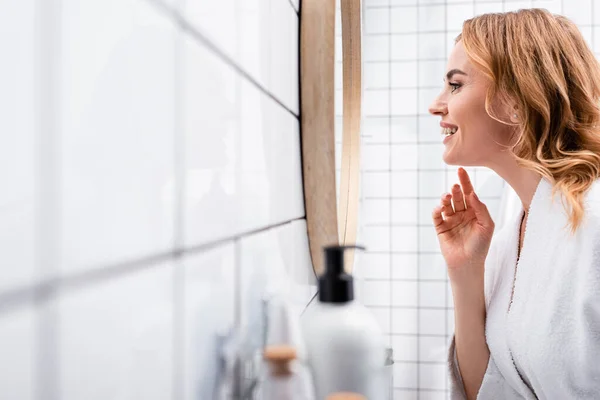 前景のぼやけた瓶の近くの鏡を見る幸せな女性の — ストック写真