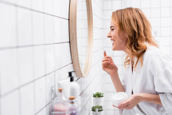 Sidovy Leende Kvinna Hålla Burk Och Applicera Ansiktskräm Medan Tittar — Stockfoto