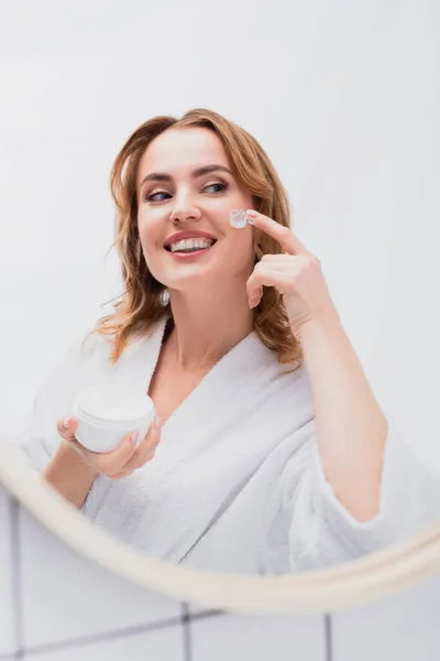 Mujer Complacida Sosteniendo Frasco Aplicando Crema Facial Mientras Mira Espejo — Foto de Stock