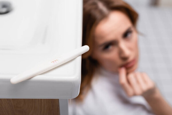 pregnancy test with positive result near worried woman on blurred background