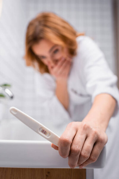 pregnancy test in hand on pregnant woman in bathrobe feeling nausea in bathroom on blurred background