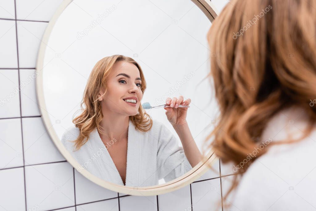 joyful woman holding toothbrush with toothpaste and looking at mirror