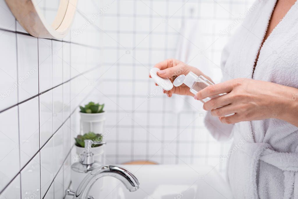 cropped view of woman holding toner and cotton pad in bathroom 