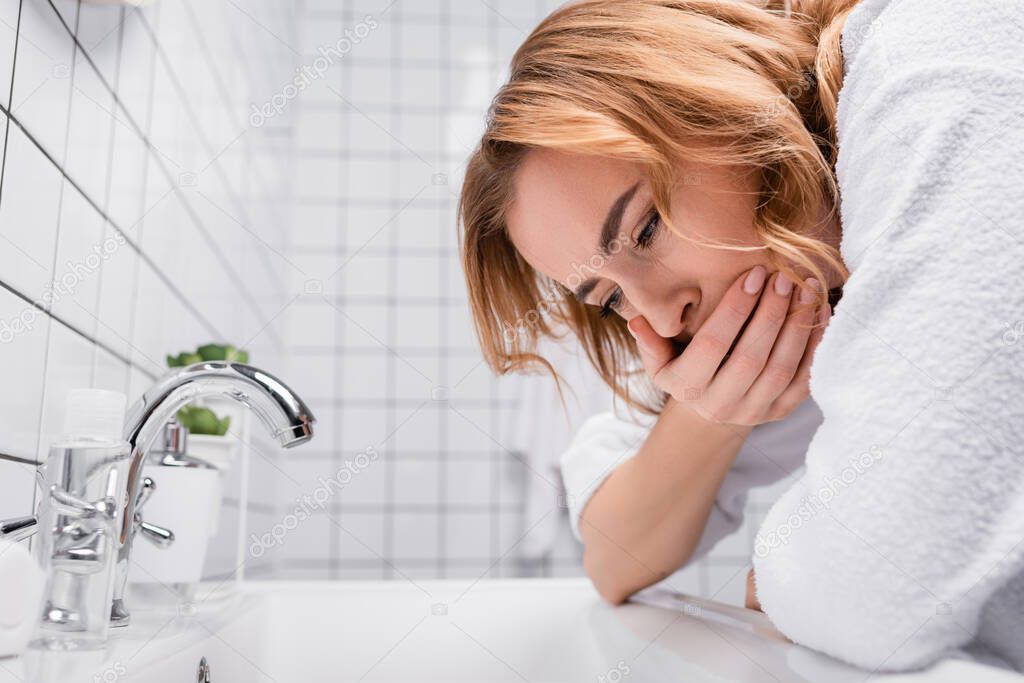 pregnant woman covering mouth while feeling nausea near sink in bathroom 