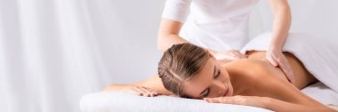 masseur massaging pleased young woman on massage table in spa salon, banner clipart