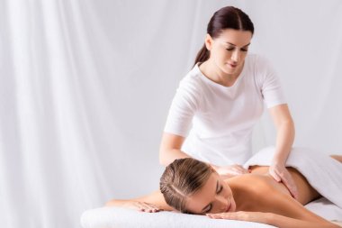 brunette masseur massaging back of woman on massage table in spa salon clipart