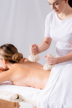 Masör, spa salonunda bitki torbalarıyla müşteriye masaj yapıyor. 