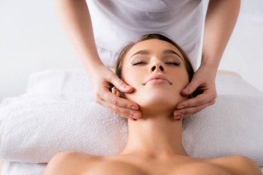 Kaplıca salonundaki müşteriye yüz masajı yapan kadın masör. 