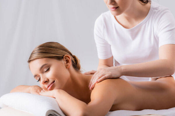 female masseur massaging pleased client lying on massage table 