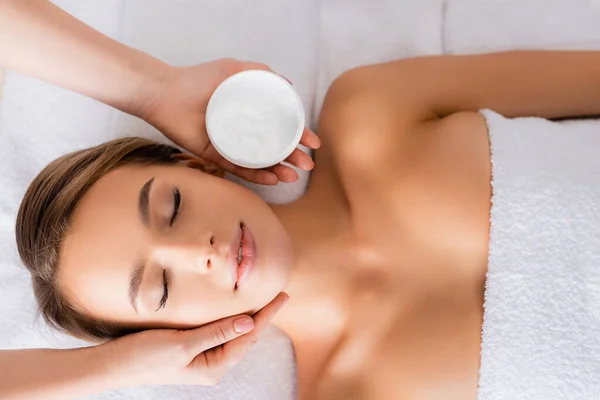 Ovanifrån Kosmetolog Hålla Behållare Med Ansiktsmask Nära Kvinna Massagebord — Stockfoto