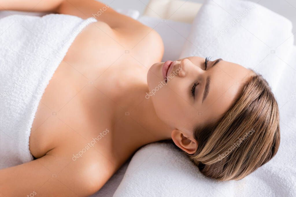 peaceful woman with closed eyes lying on massage table in spa salon